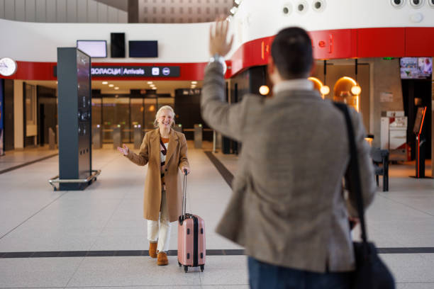 Une femme fait signe à un homme dans le hall des arrivées de l'aéroport.